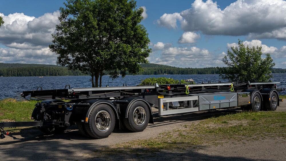En lastbil med en liftdumper som kör längs en väg med gröna träd i bakgrunden